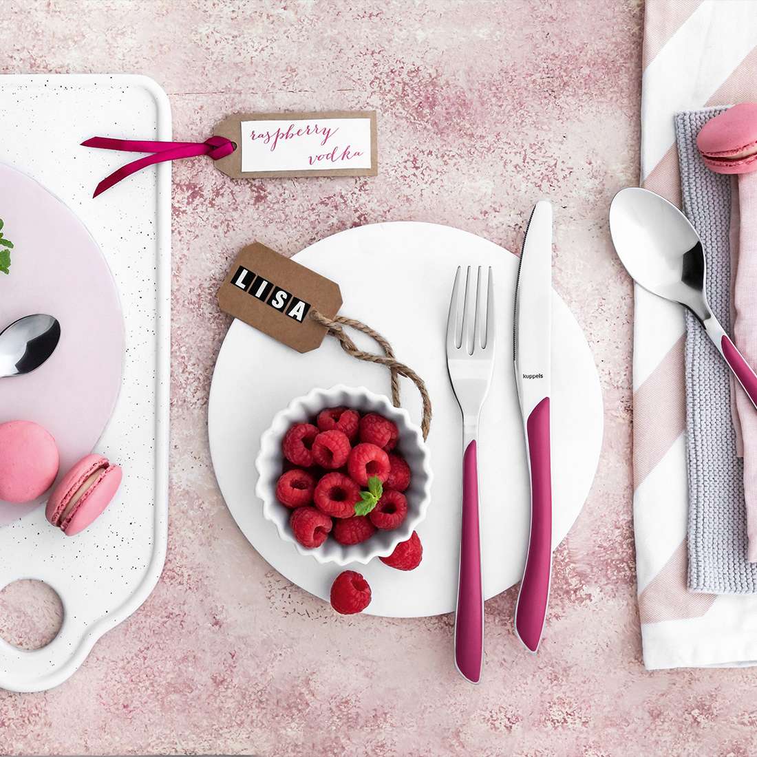 Ein gedeckter Tisch mit Himbeeren, Macarons, Namensschildern für LIISA und die Himbeerwoche, einer Serviette und Kuppels PRISMA Kuchengabel-Set 6-teilig himbeerrotes Besteck auf einem Hintergrund mit Himbeerrot-Motiven.
