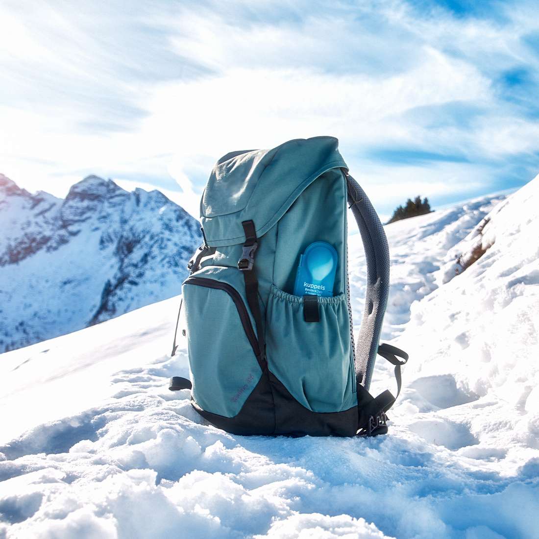 Ein blaugrüner Rucksack mit einem 4-teiligen Kuppels 2GO Besteckset in Mint in der Seitentasche liegt auf Schnee, umgeben von Berggipfeln und blauem Himmel – eine platzsparende, nachhaltige Wahl für Ihre Outdoor-Abenteuer.