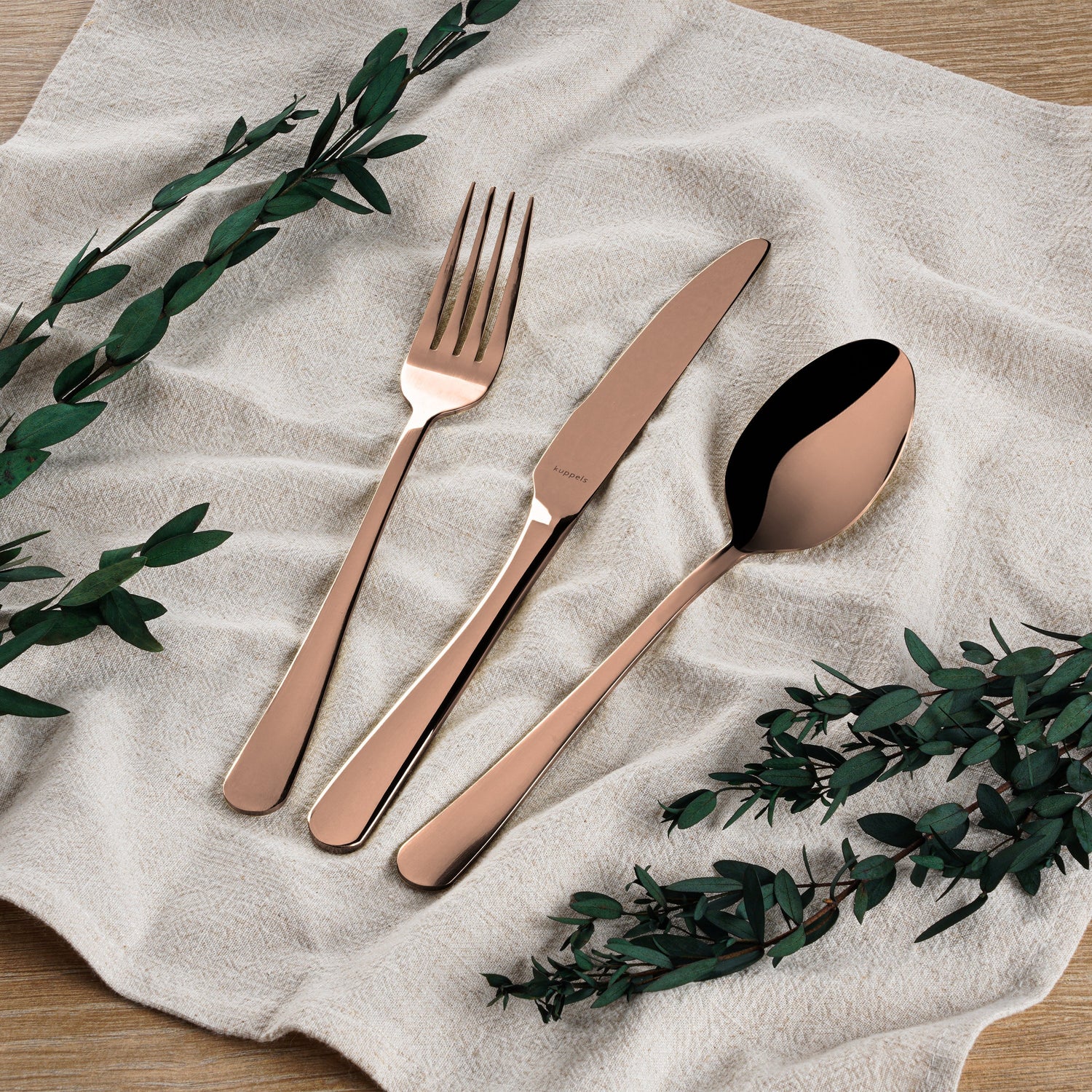 Ein blaugrüner Teller mit einer Gabel, einem Messer und einer Dessertgabel auf einem hölzernen Ladegerät mit einer beigen Serviette und getrockneten Blättern vor einem dunklen Hintergrund.