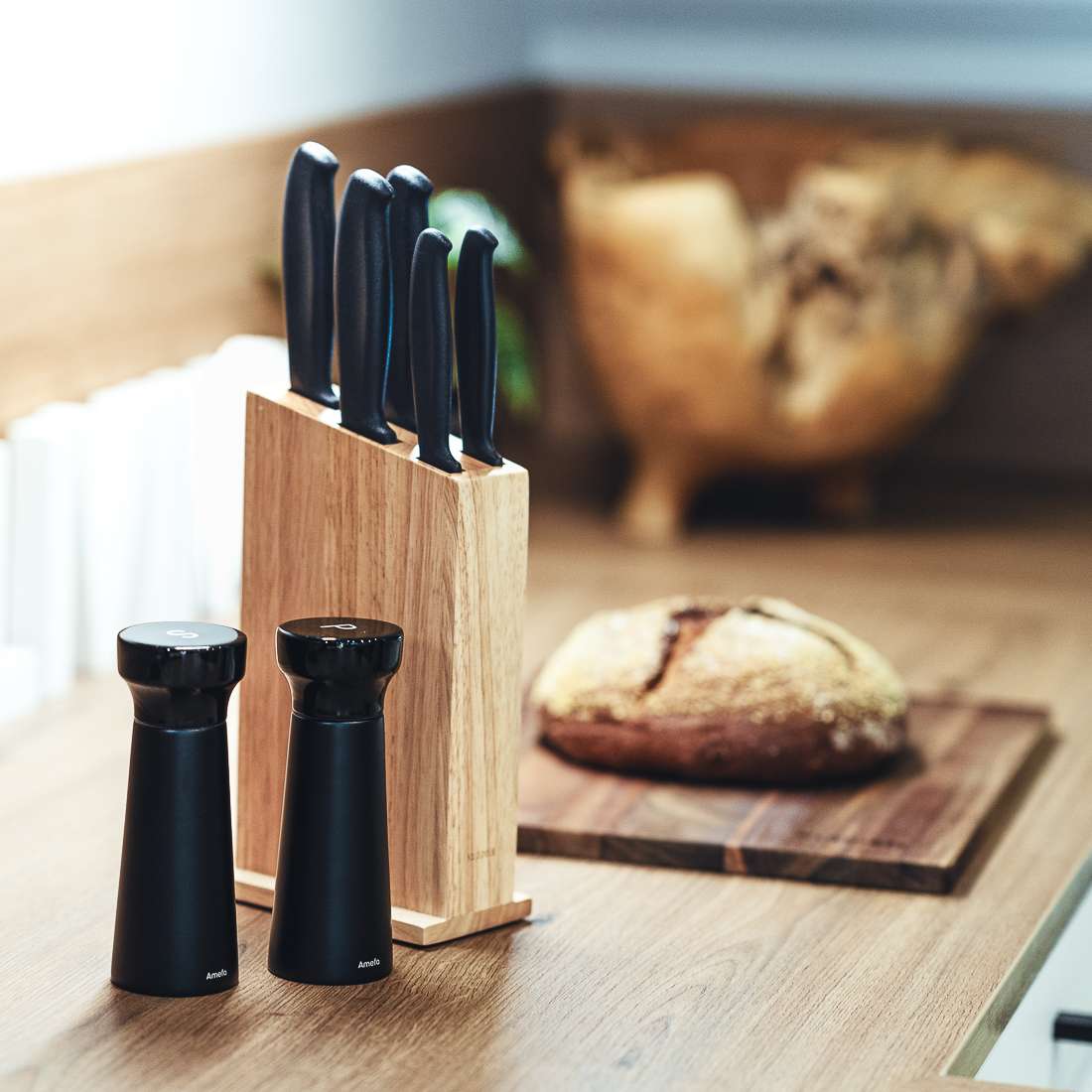 Ein Kuppels BASIC Messerblock 5-teilig, zwei schwarze Salz- und Pfeffermühlen und ein Laib Brot auf einem Holzschneidebrett schmücken die Küchentheke.