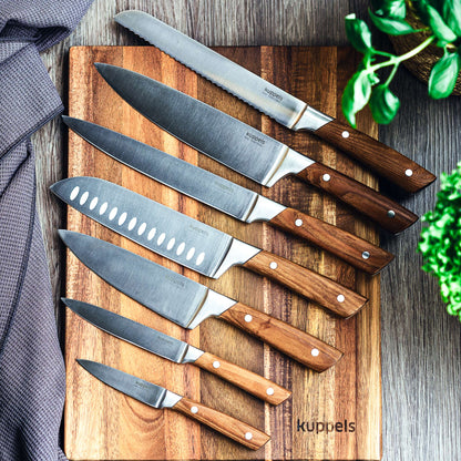 Ein Set aus sieben AVID-Gemüsemessern von Kuppels mit eleganten Griffen aus Eschenholz ist wunderschön auf einem Holzschneidebrett mit der Aufschrift „kuppels“ arrangiert, ergänzt durch ein graues Tuch und grüne Pflanzen. Diese aus strapazierfähigem 50CrMoV15-Stahl gefertigten Messer – darunter ein vielseitiges Spickmesser – vereinen Stil und Präzision für Ihre Küche.