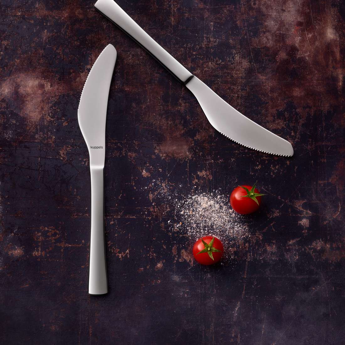 Zwei SELECTION Pizzamesser von Kuppels liegen auf dunkler, strukturierter Fläche neben etwas Salz und zwei reifen Cherrytomaten mit grünen Stielen.