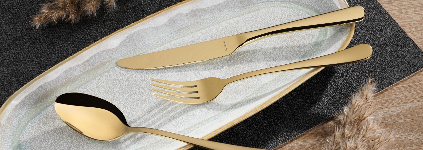 Goldenes Besteckset, Messer, Gabel, Löffel auf ovalem Teller mit Goldrand